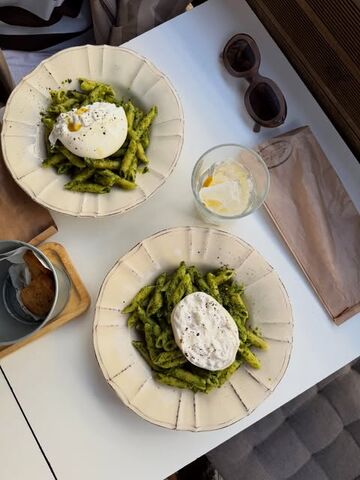 Dois pratos de penne ao pesto com burrata numa mesa branca da esplanada