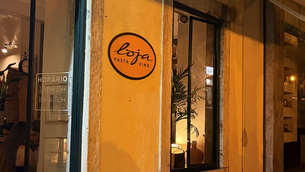 A fachada à noite: a porta verde, a placa oval com loja escrito à mão e a janela iluminada