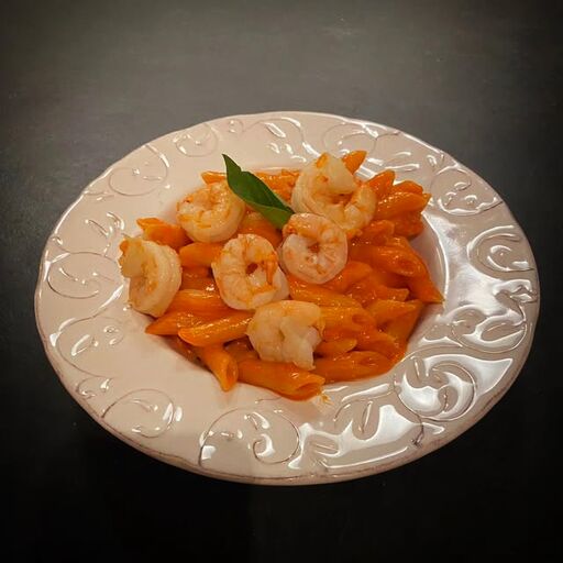 Penne num molho cor de laranja com camarões e uma folha de manjericão