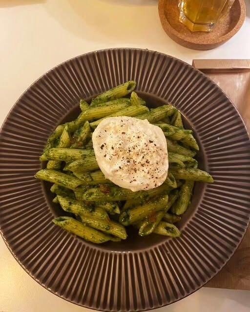 Penne ao pesto com uma burrata inteira por cima, num prato canelado