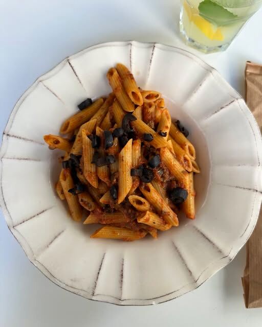 Penne com molho de tomate e azeitonas pretas num prato branco